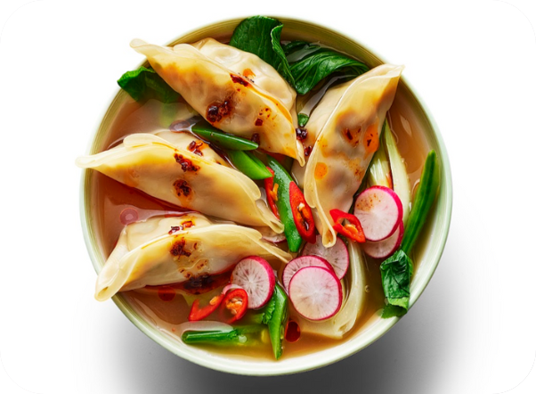 A bowl of dumpling soup with bok choy, sliced radishes, and red chilies.