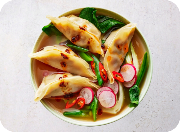 Bowl of savory dumpling soup with bok choy, green beans, radishes, and chili.
