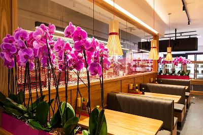 Vibrant pink orchid arrangement dividing wooden tables and booth seating in a modern restaurant interior.