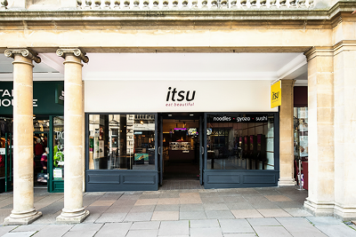 Itsu restaurant storefront with prominent logo, 'eat beautiful' slogan, and classical stone columns.