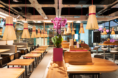 Modern restaurant interior with wooden tables, booths, and unique wicker-like pendant lights.