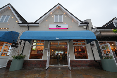 Storefront of Itzu with a blue awning, open doors, and festive string lights.