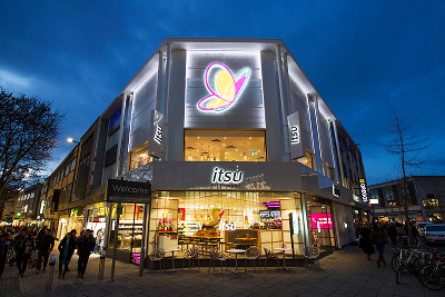 Modern retail store at night with a large glowing butterfly logo and "itsu" sign.