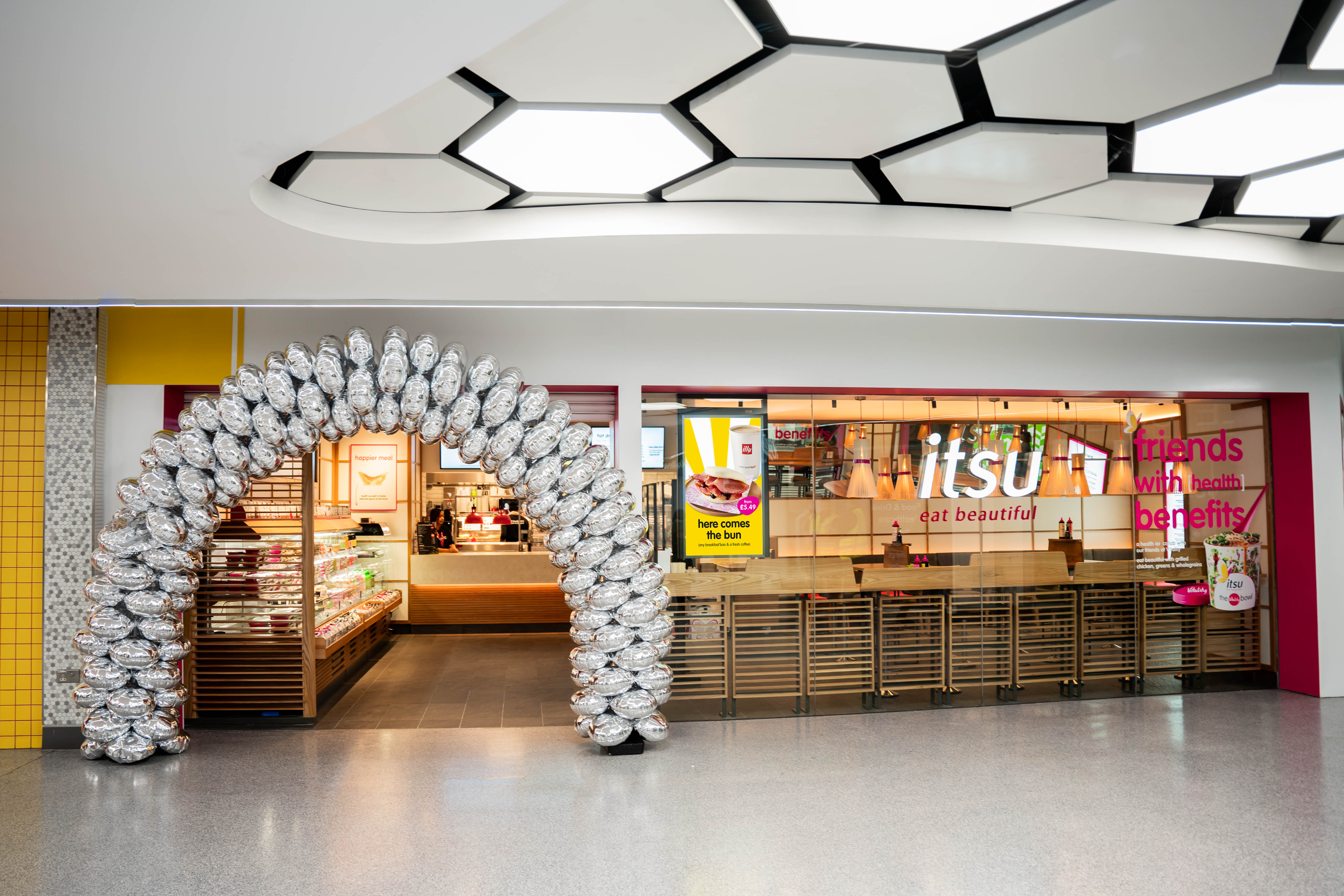 Itsu sushi shop entrance with a festive white balloon arch and hexagon ceiling lights.