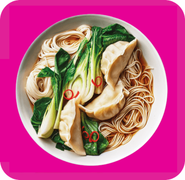 A bowl of noodle soup with dumplings, bok choy, and red chili slices in broth.