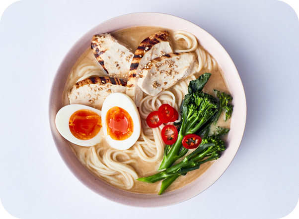 Creamy chicken ramen bowl with noodles, soft-boiled eggs, broccoli, and tomatoes.