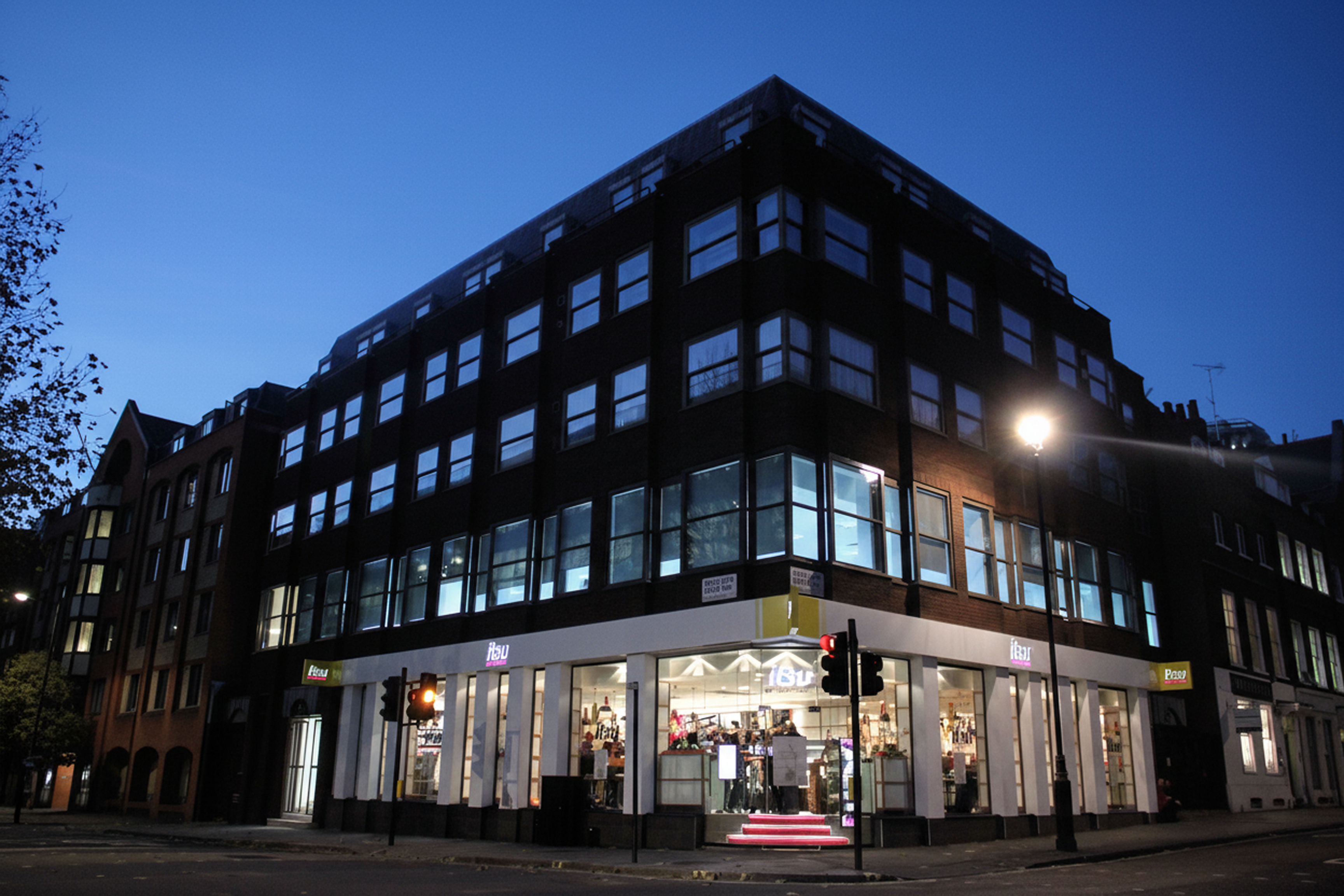 Brightly lit retail store on the ground floor of a corner building at night.