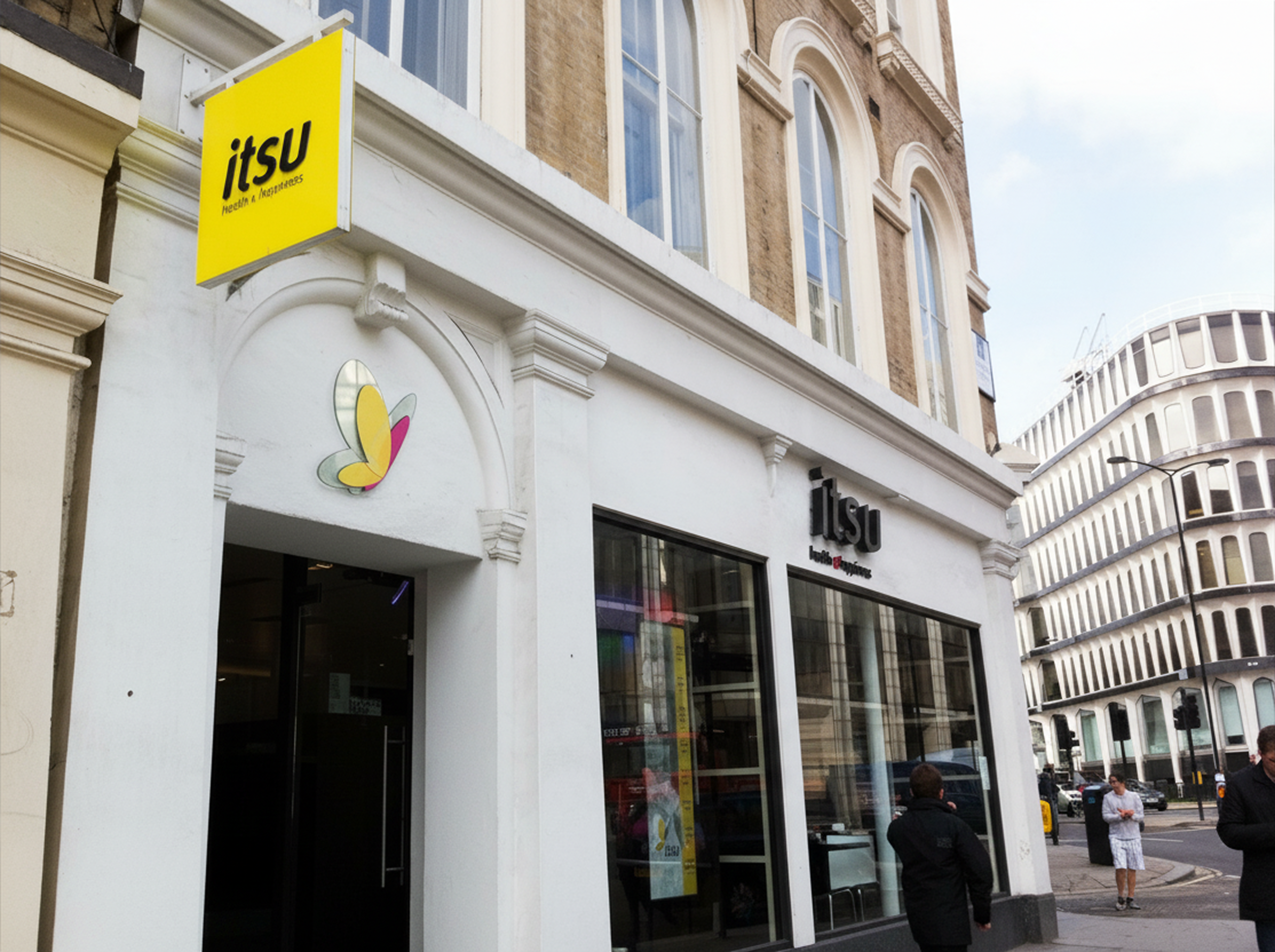 itsu restaurant storefront with a bright yellow sign and butterfly logo on a city street.