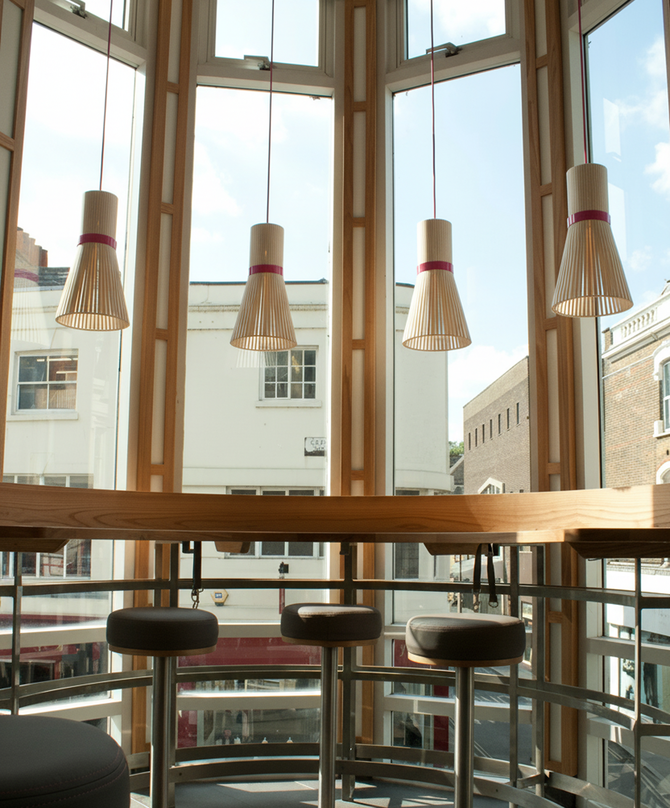 Modern interior with pendant lights, bar stools, and large windows overlooking urban buildings.