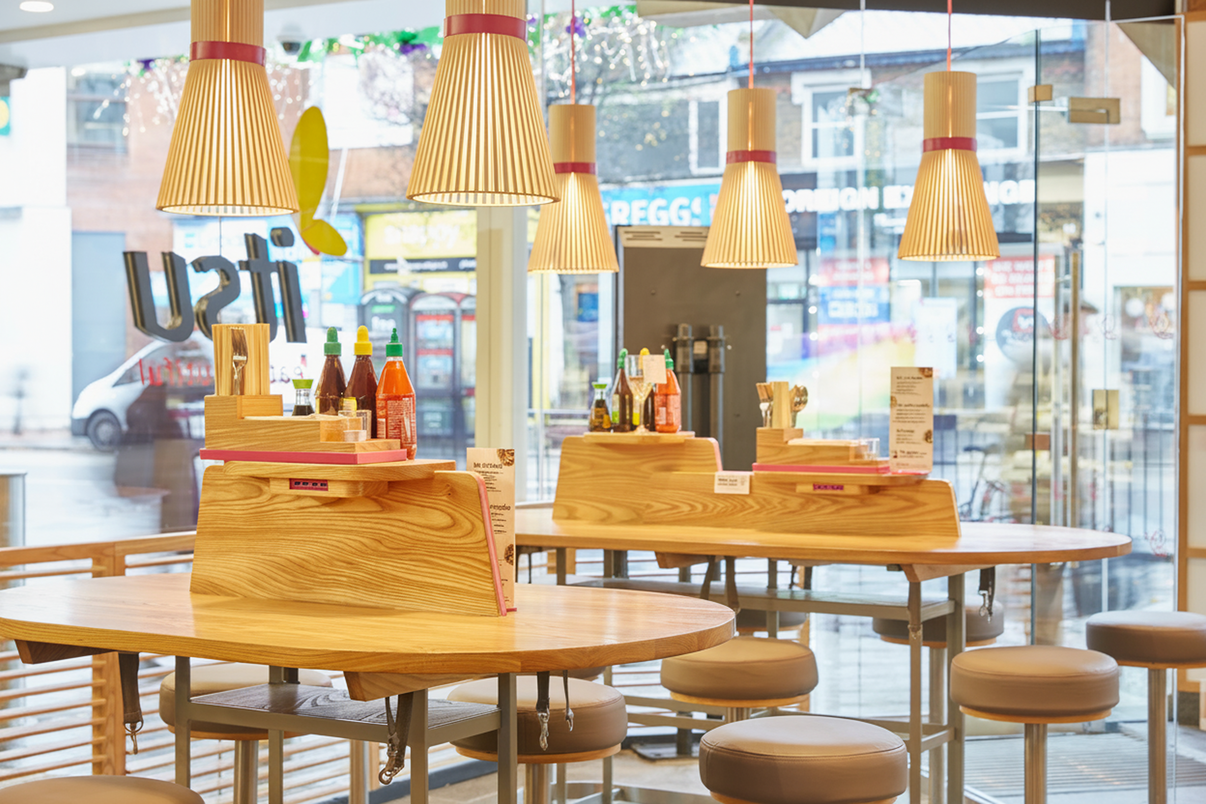 Modern itsu restaurant interior with light wood tables, stools, and stylish pendant lights.