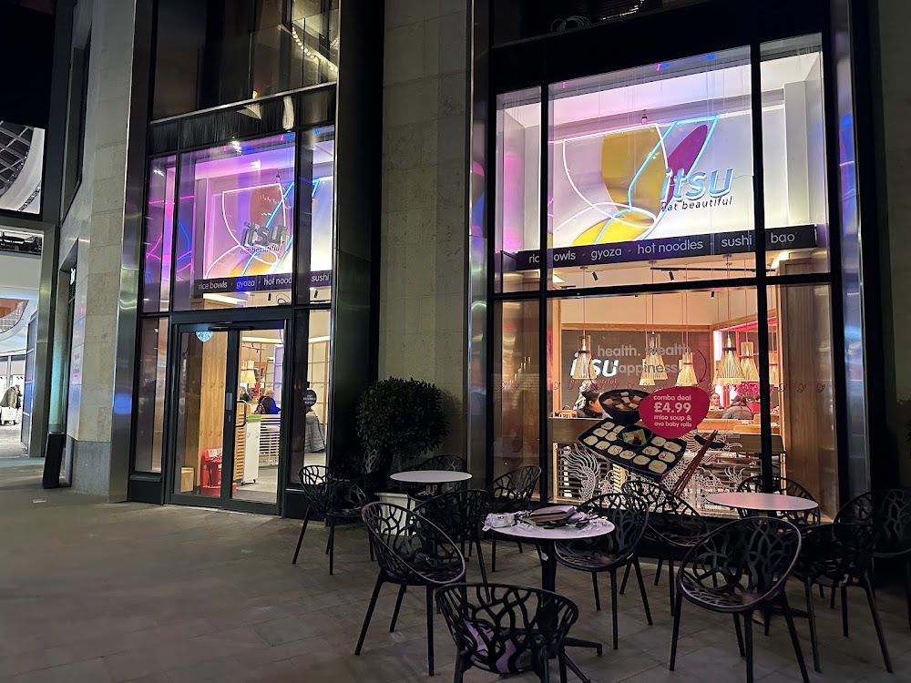 Modern building exterior at night with illuminated window displays and outdoor cafe seating.