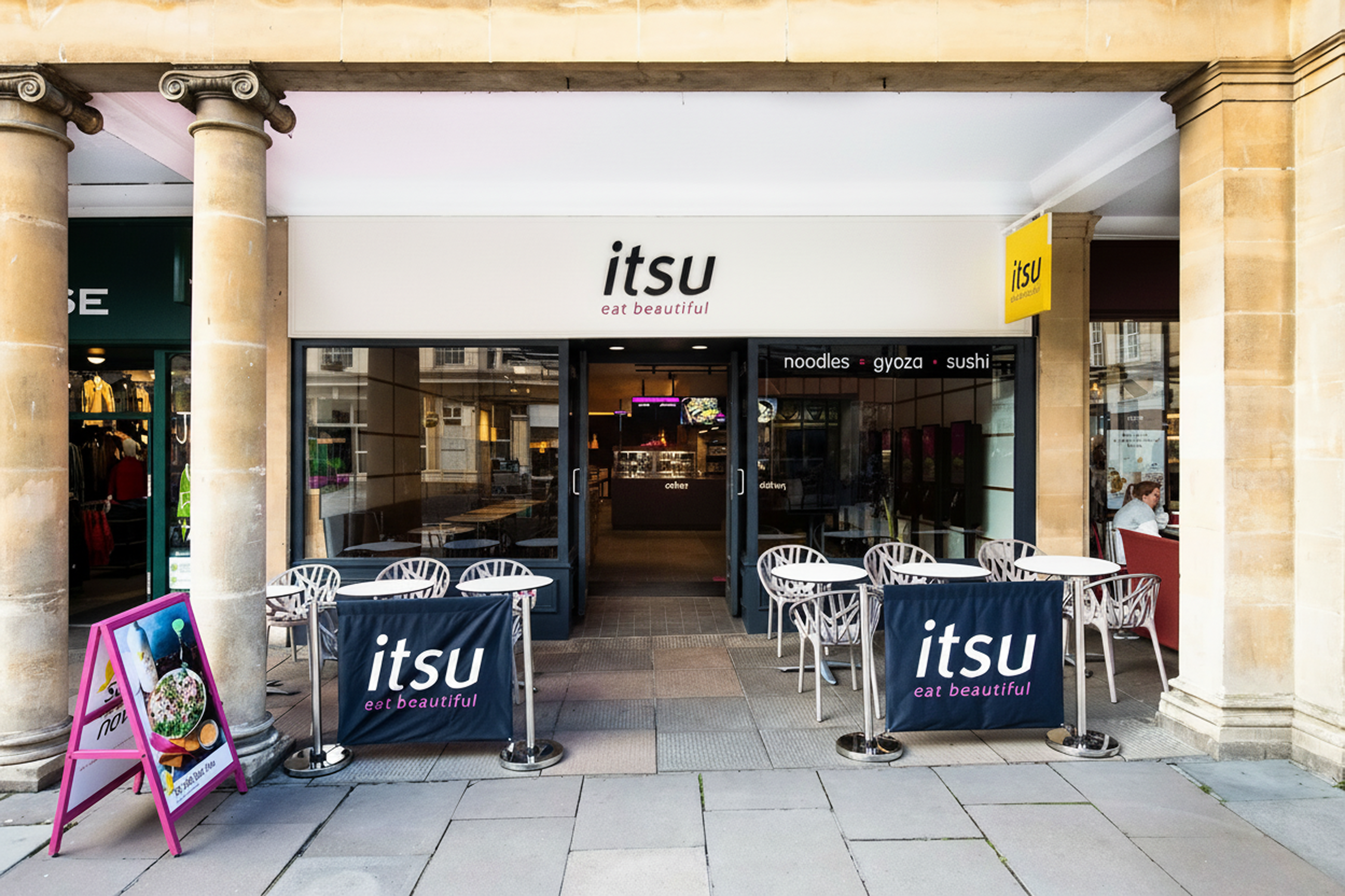 itsu restaurant exterior with outdoor seating under a stone arcade, bright daytime.