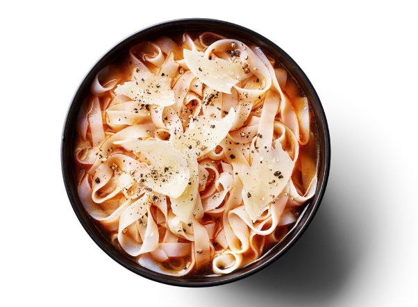 Bowl of tagliatelle pasta with tomato sauce, shaved Parmesan, and black pepper.