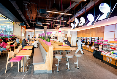 Bright modern cafe interior with customers, pink chairs, and butterfly light fixtures.