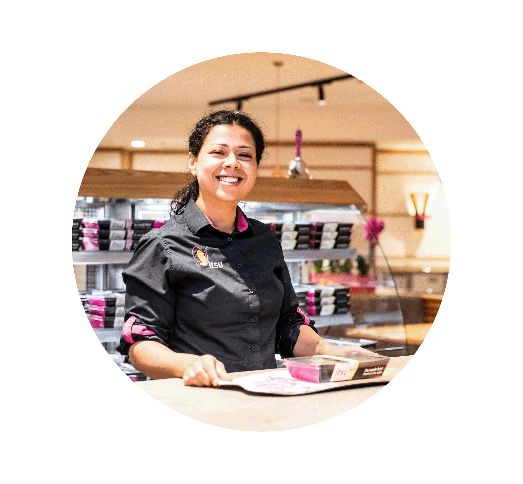 Smiling woman behind a store counter, wearing a dark uniform shirt.