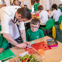 Chef helps a young boy chop tomatoes during a cooking class lesson.