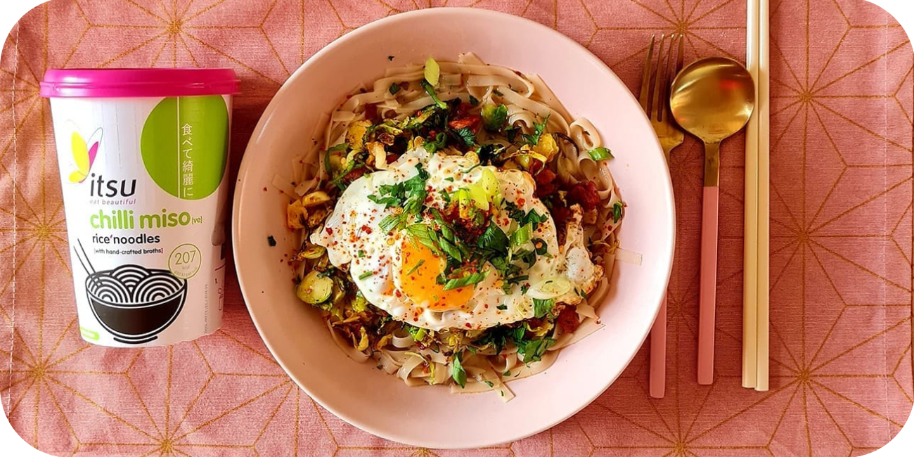 Bowl of chilli miso rice noodles with a fried egg, next to an Itsu container.