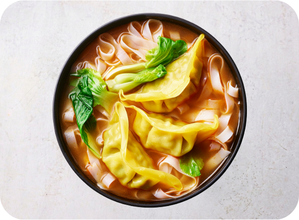 Hot wonton noodle soup with bok choy in a black bowl on a light surface.
