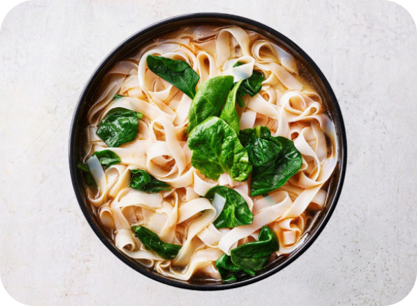 A bowl of wide flat noodles with vibrant green spinach leaves in a light broth.