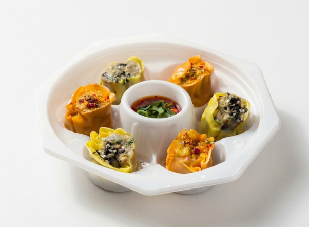 Six colorful dumplings (dim sum) with a central dipping sauce on a white octagonal dish.
