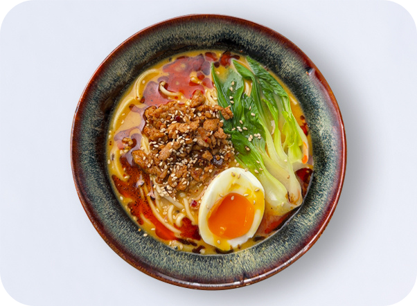 Spicy ramen bowl with noodles, ground meat, soft-boiled egg, and green vegetables.