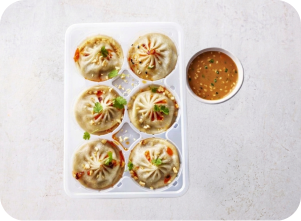 Six steamed dumplings garnished with herbs and a side of chili dipping sauce.