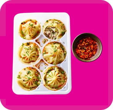 Six delicious soup dumplings in a white tray with a side of spicy chili oil.