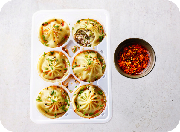 Six delicious dumplings topped with chili oil and fresh herbs, next to a bowl of sauce.