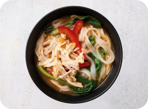 Chicken noodle soup with red peppers and green vegetables in a black bowl.