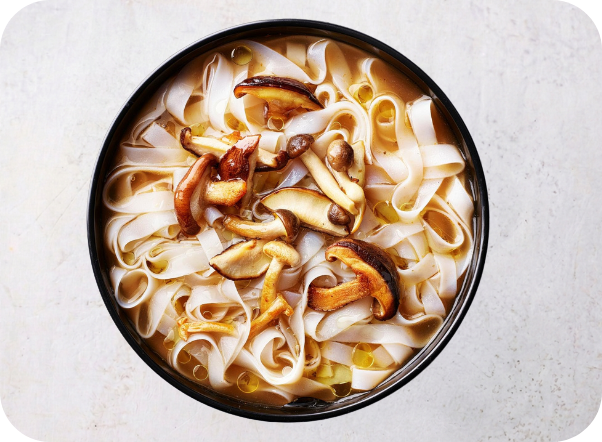 A black bowl filled with flat rice noodles, sliced shiitake mushrooms, and clear broth.