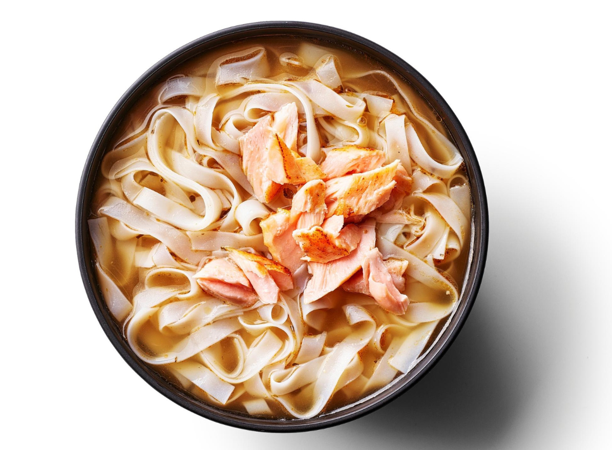 Bowl of wide rice noodles with flaked salmon in a clear, light broth.