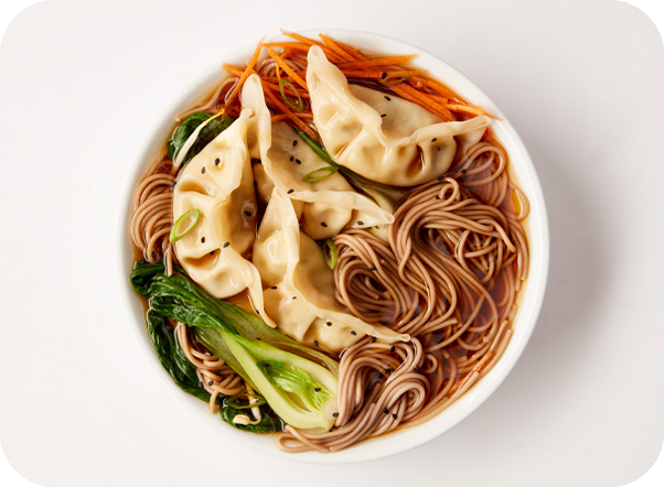 A white bowl of savory ramen with dumplings, soba noodles, bok choy, and carrots.
