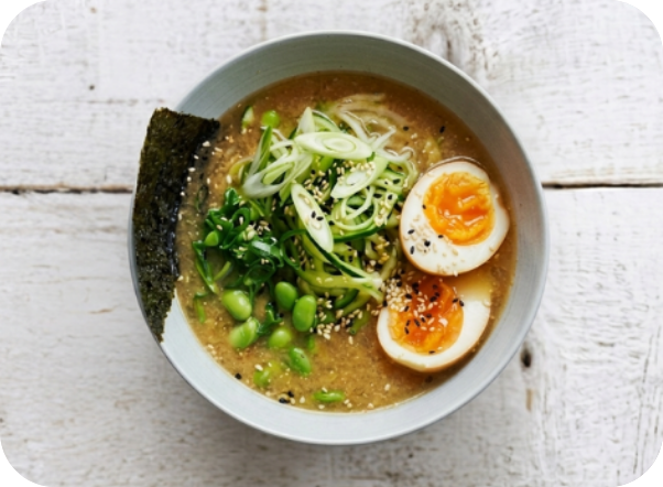 Bowl of ramen with zucchini noodles, edamame, soft-boiled eggs, and green onions.
