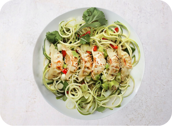 Overhead view of pan-fried dumplings atop zucchini noodles with chili and cilantro garnish.