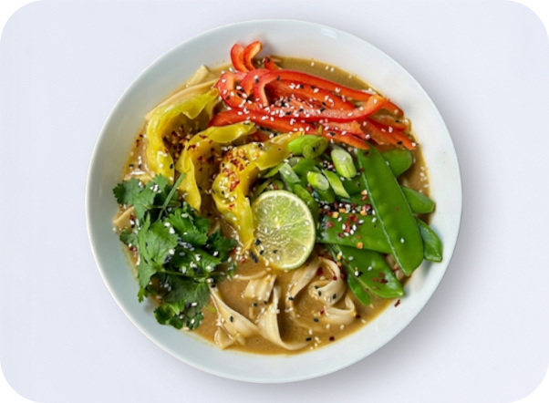 A colorful bowl of ramen noodles topped with bell peppers, snow peas, cilantro, and lime.