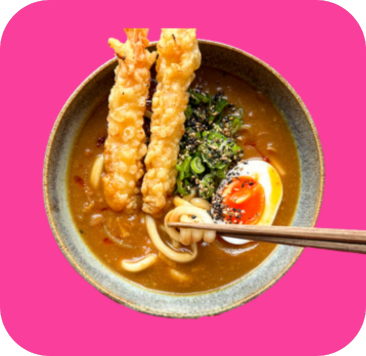 A bowl of Japanese curry udon noodles with tempura shrimp, a soft-boiled egg, and chopsticks.