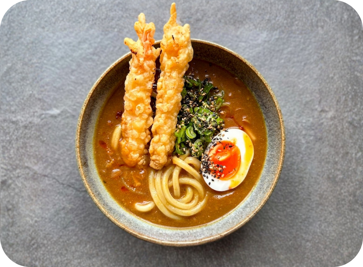 Udon noodles with tempura shrimp, soft-boiled egg, and rich curry broth in a ceramic bowl.