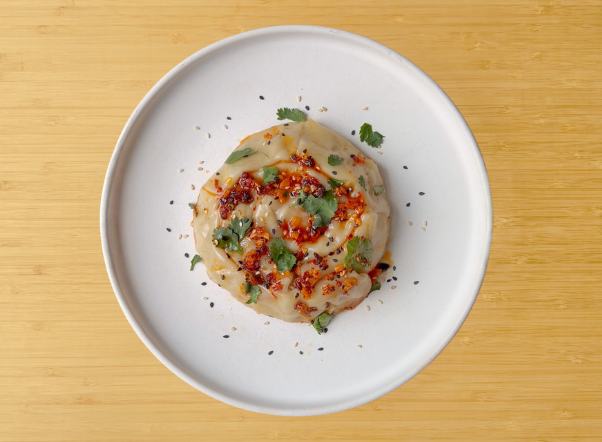 Savory spiral bun topped with chili oil, black sesame seeds, and fresh cilantro on a white plate.