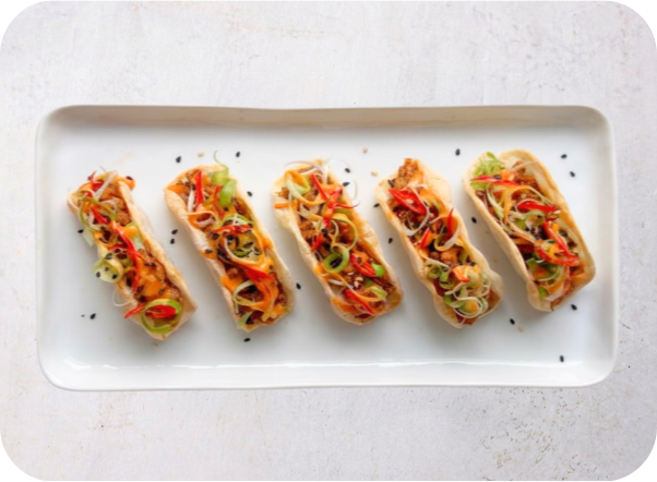 Five mini tacos filled with colorful shredded meat and fresh vegetables on a white plate.