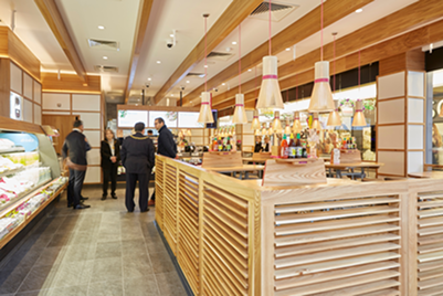 Modern restaurant interior with a long wooden counter, food displays, and several patrons.