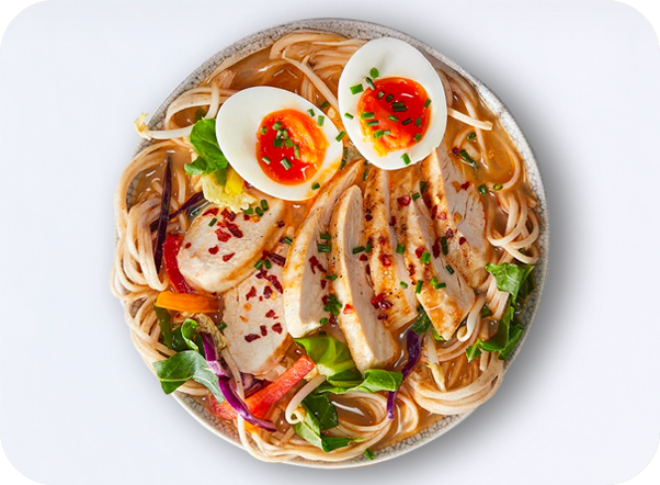 Bowl of chicken ramen with soft-boiled eggs, noodles, and fresh colorful vegetables.