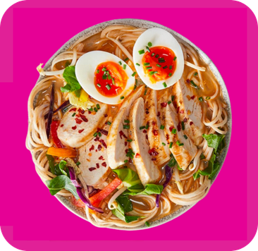Bowl of chicken ramen with soft-boiled eggs, noodles, and fresh vegetables garnished with chili.