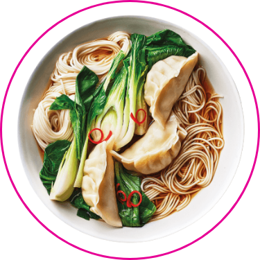 A bowl of noodle soup with dumplings, bok choy, and red chili slices.