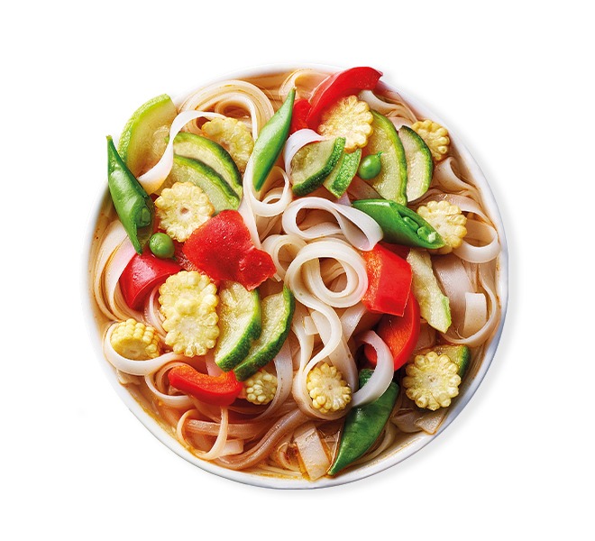Colorful bowl of rice noodle soup with red peppers, baby corn, and green vegetables.