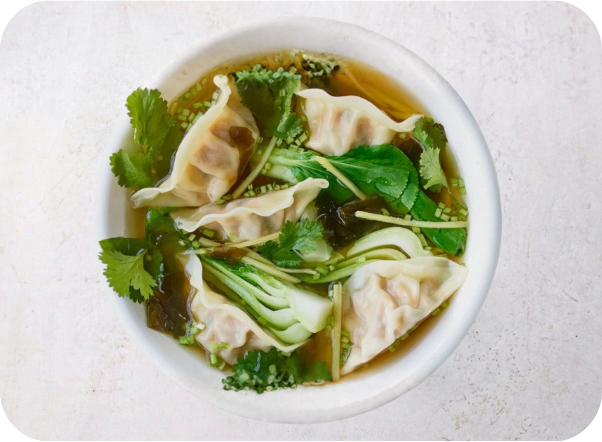 Bowl of dumpling soup with bok choy and cilantro, seen from above.