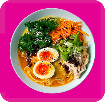 Colorful bowl of ramen with eggs, chicken, kale, shredded carrots, and green onions.