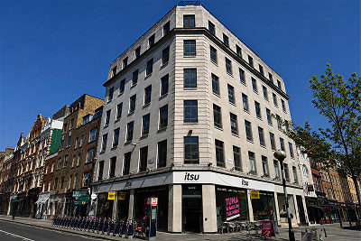 Light-colored corner building with multiple floors and 'itsu' store signs at street level.
