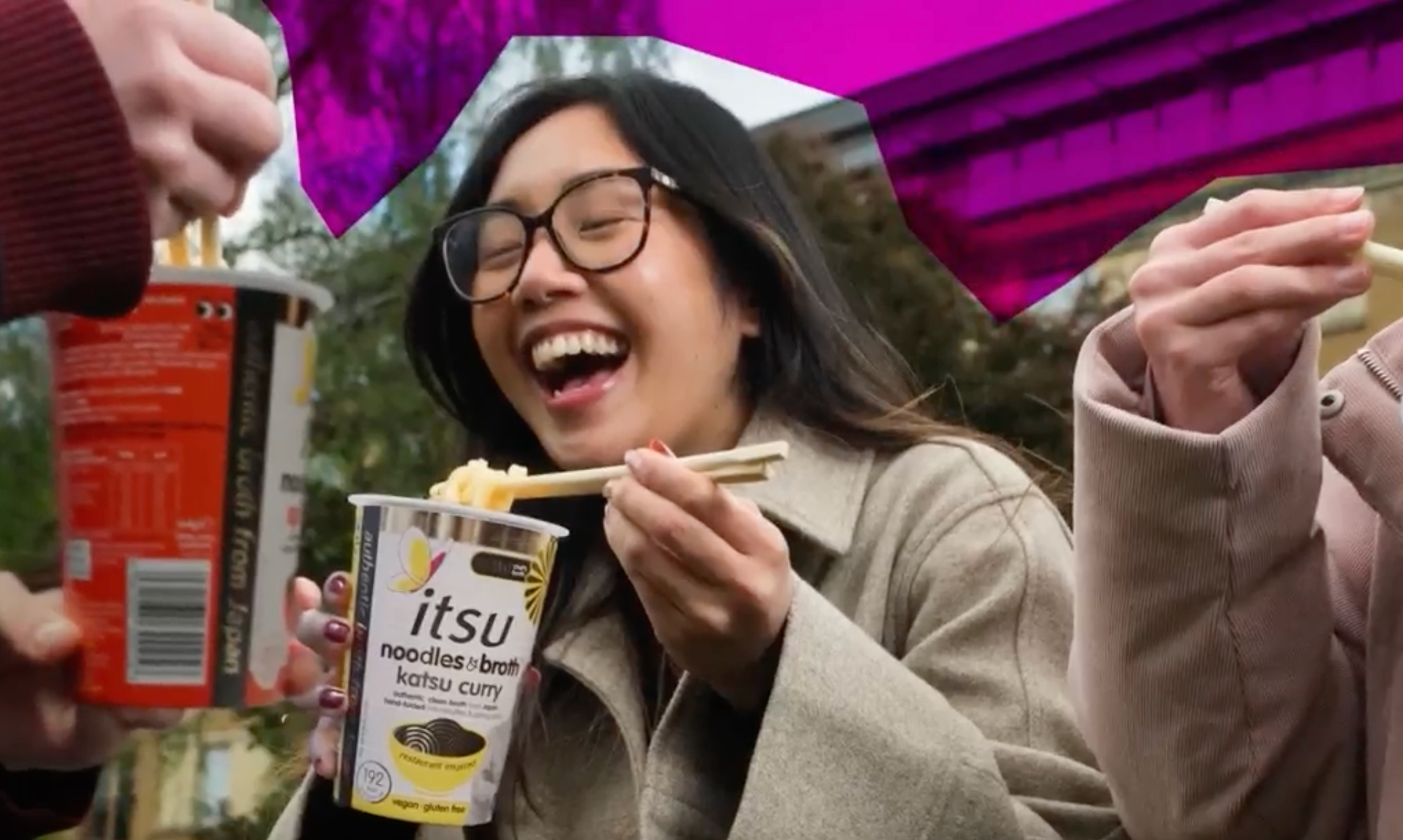 Joyful woman laughing while eating instant noodles with chopsticks outdoors.