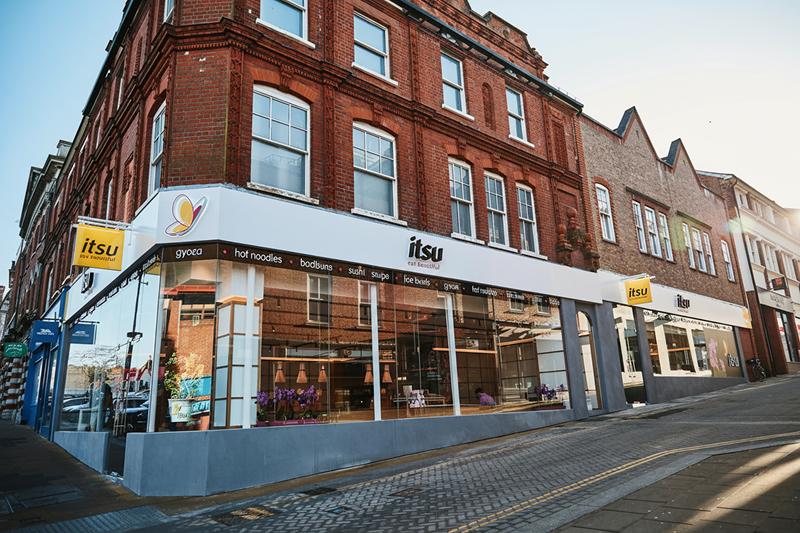 Itsu restaurant on a corner of a red brick building with large windows.