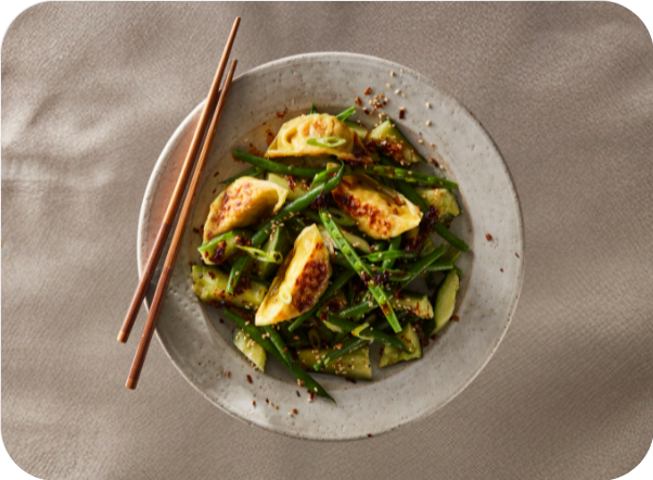 Pan-fried dumplings, green beans, and cucumber salad with chopsticks on a plate.